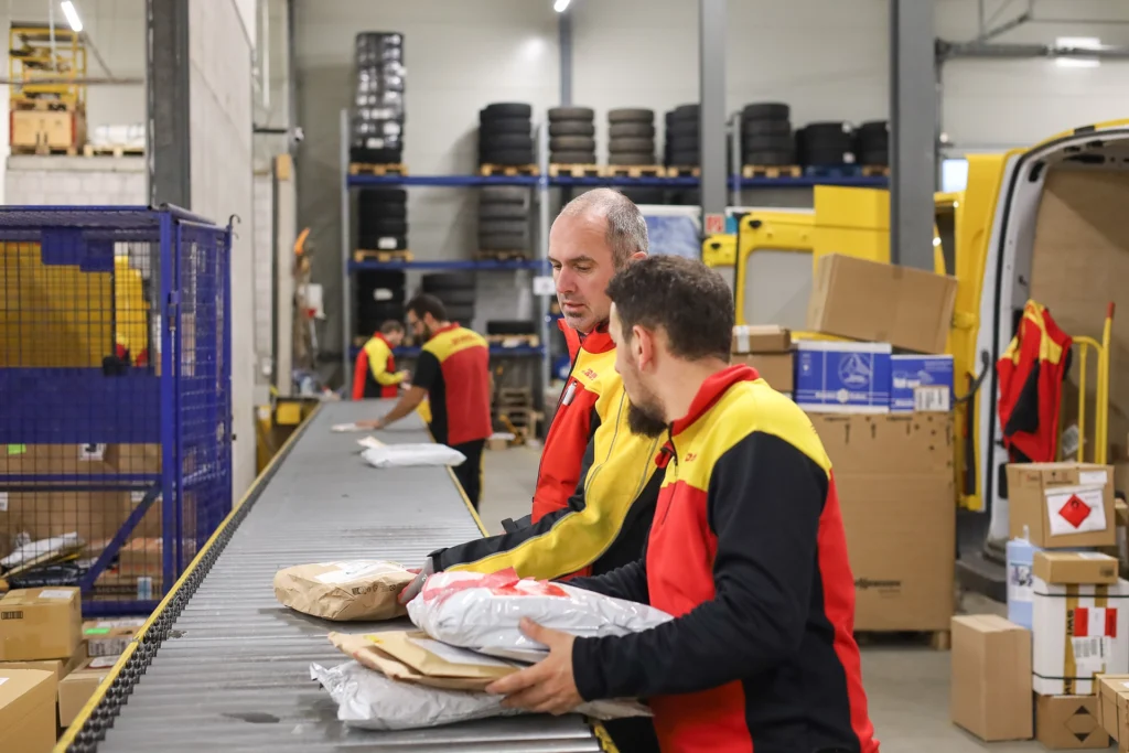 DHL Mitarbeiter sortieren Pakete in Speditionshalle